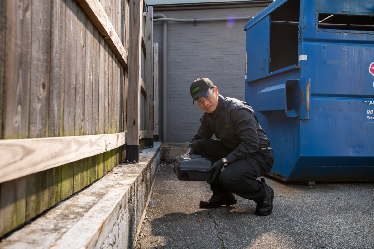 Terminix technician installing a rat station near retail stores dumpsters