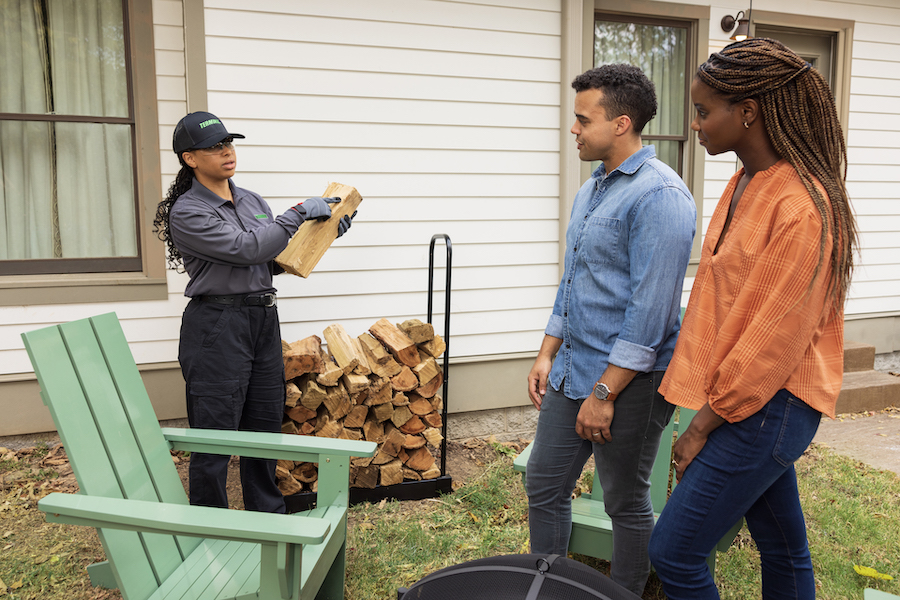 Terminix tech talking to couple holding a piece of fire wood
