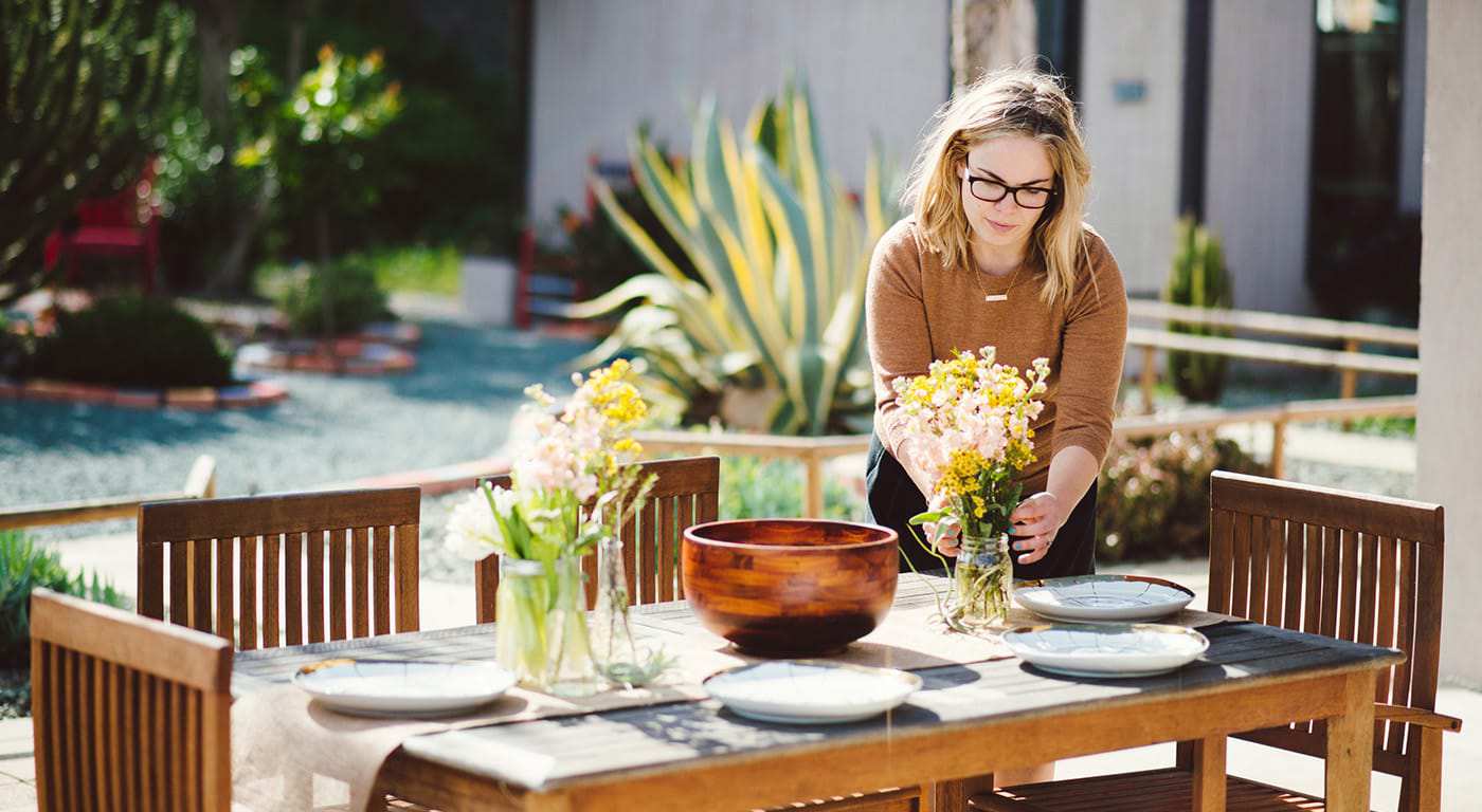Woman standing at an outdoor dinner table arranging flowers 