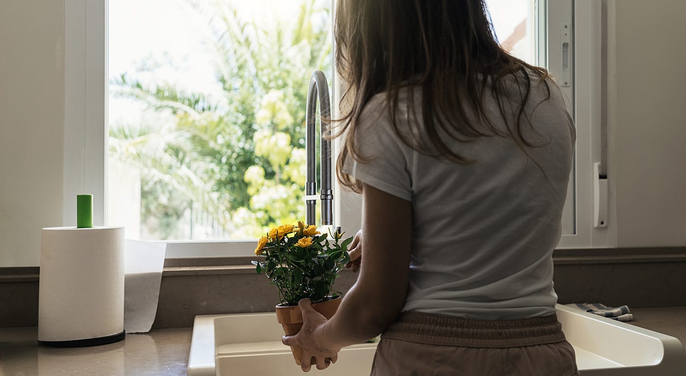 Woman standing at kitchen sink watering a plant