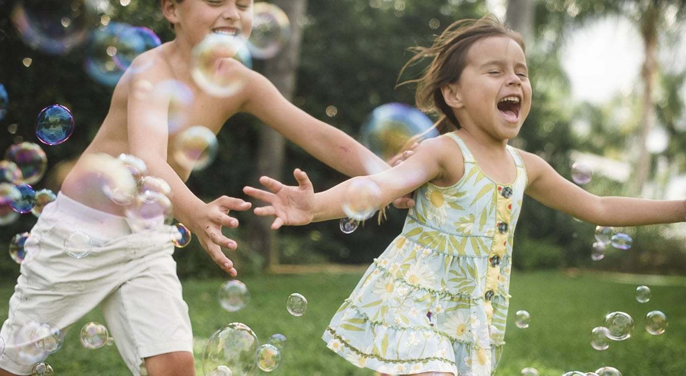 2 young children chasing each other outside with bubbles