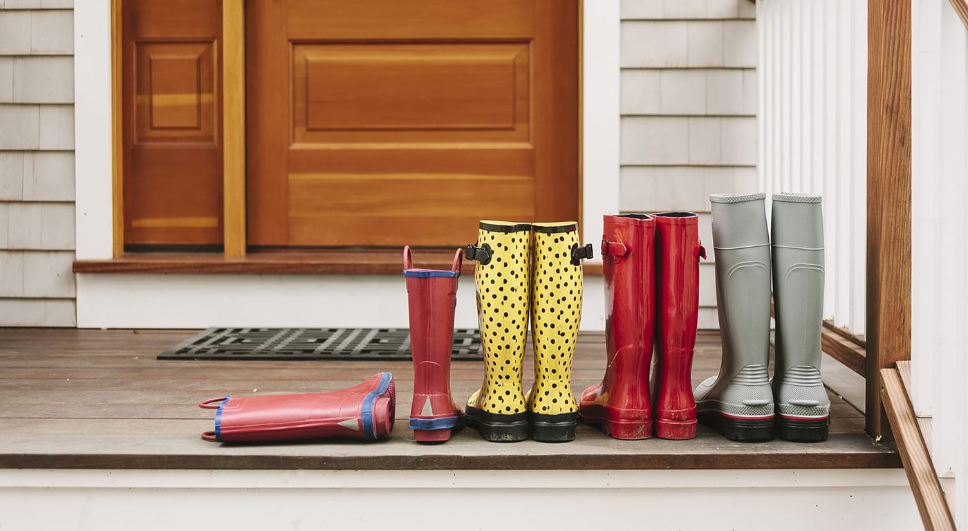 Four sets of rain boots (adult to child size) lined up on a front porch