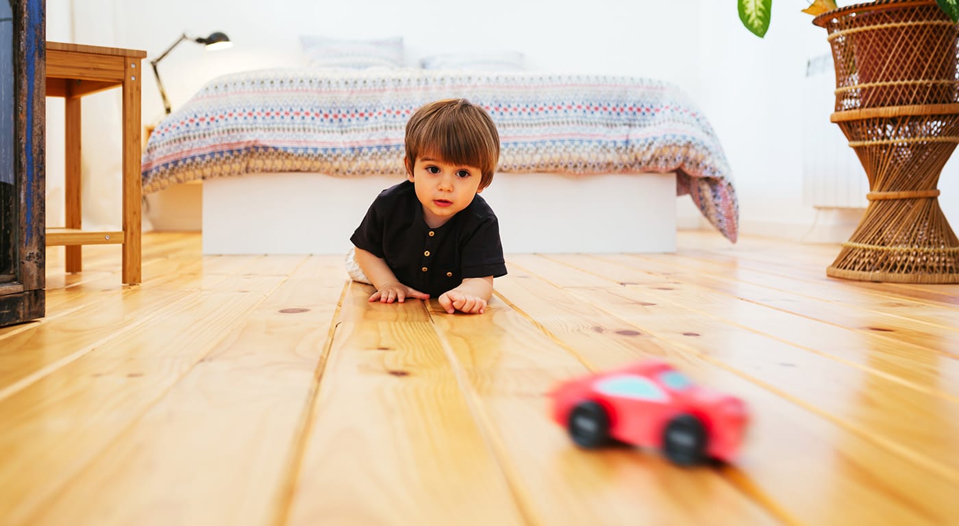 Little boy laying on the hardwood floor of bedroom playing with red toy car