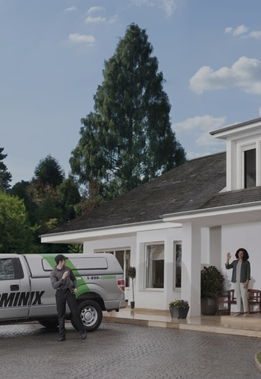 Terminix technician and customer standing in front of a Terminix truck parked in a house's driveway